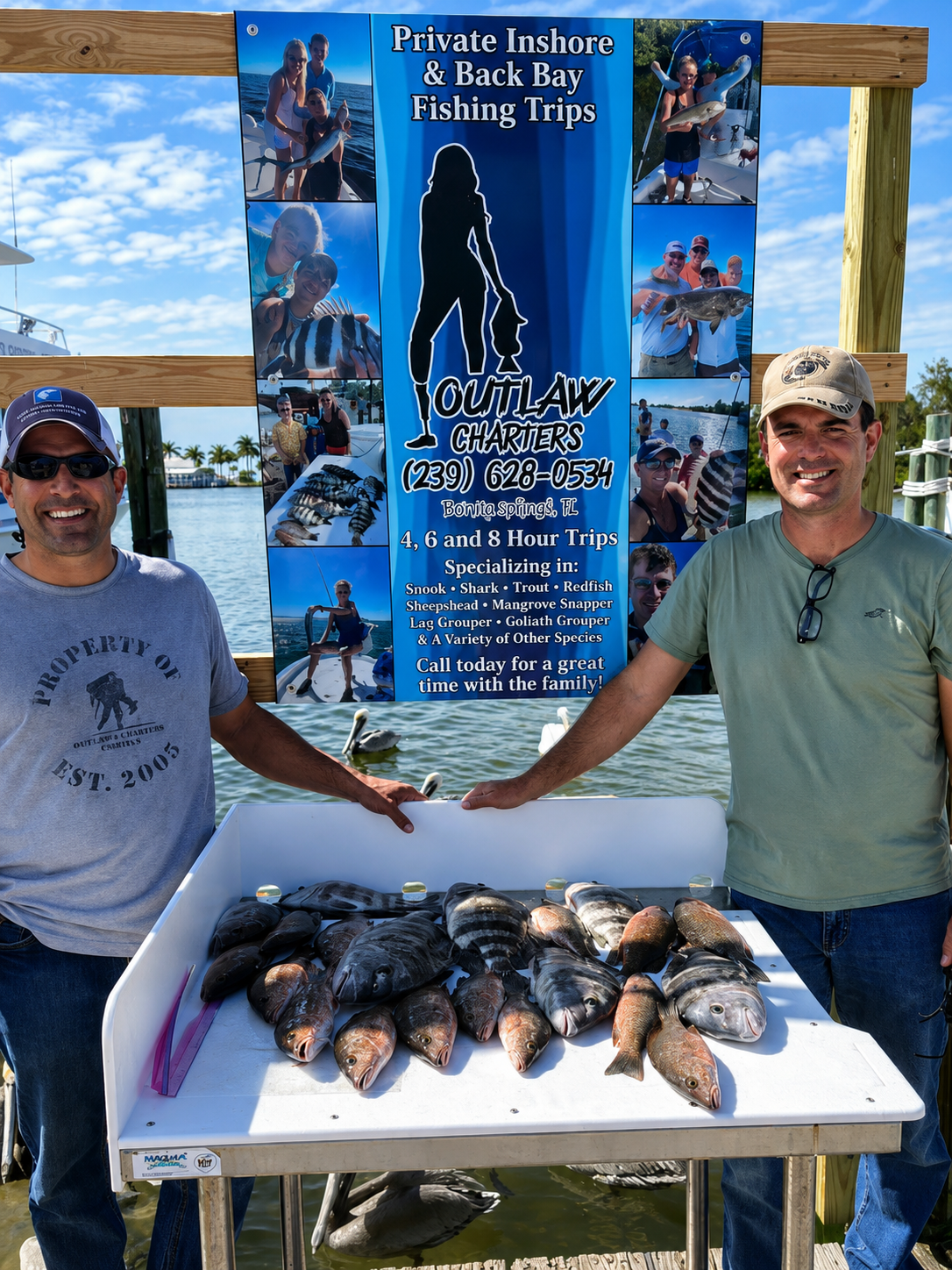 Two anglers at the Outlaw Charters banner with a full cleaning table